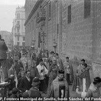 El fotógrafo Cecilio Sánchez del Pando, subido a la columna, es testigo del paso de la procesión por las gradas de la catedral. En el ángulo inferior izquierdo asoma también la figura del reportero gráfico Juan José Serrano. La escena es recogida por la cámara de Gelán. 1928 ©ICAS-SAHP, Fototeca Municipal de Sevilla, fondo Sánchez del Pando