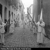 Nazarenos de luz de la Hermandad de la Candelaria por la calle San José junto al convento de Madre de Dios. Entre 1925 y 1927 y debido a la estrechez de las calles, la cofradía iba y regresaba de la Carrera Oficial por los Jardines de Murillo ©ICAS-SAHP, Fototeca Municipal de Sevilla, fondo Serrano