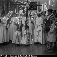 Nazarenos de la hermandad de los Gitanos portando la Cruz de Guía, el Senatus y bocinas en la calle Francos. Los nazarenos lucen ya las nuevas túnicas con capa blanca y antifaz de terciopelo estrenado en 1929. 1929-1931 ©ICAS-SAHP, Fototeca Municipal de Sevilla, fondo Serrano
